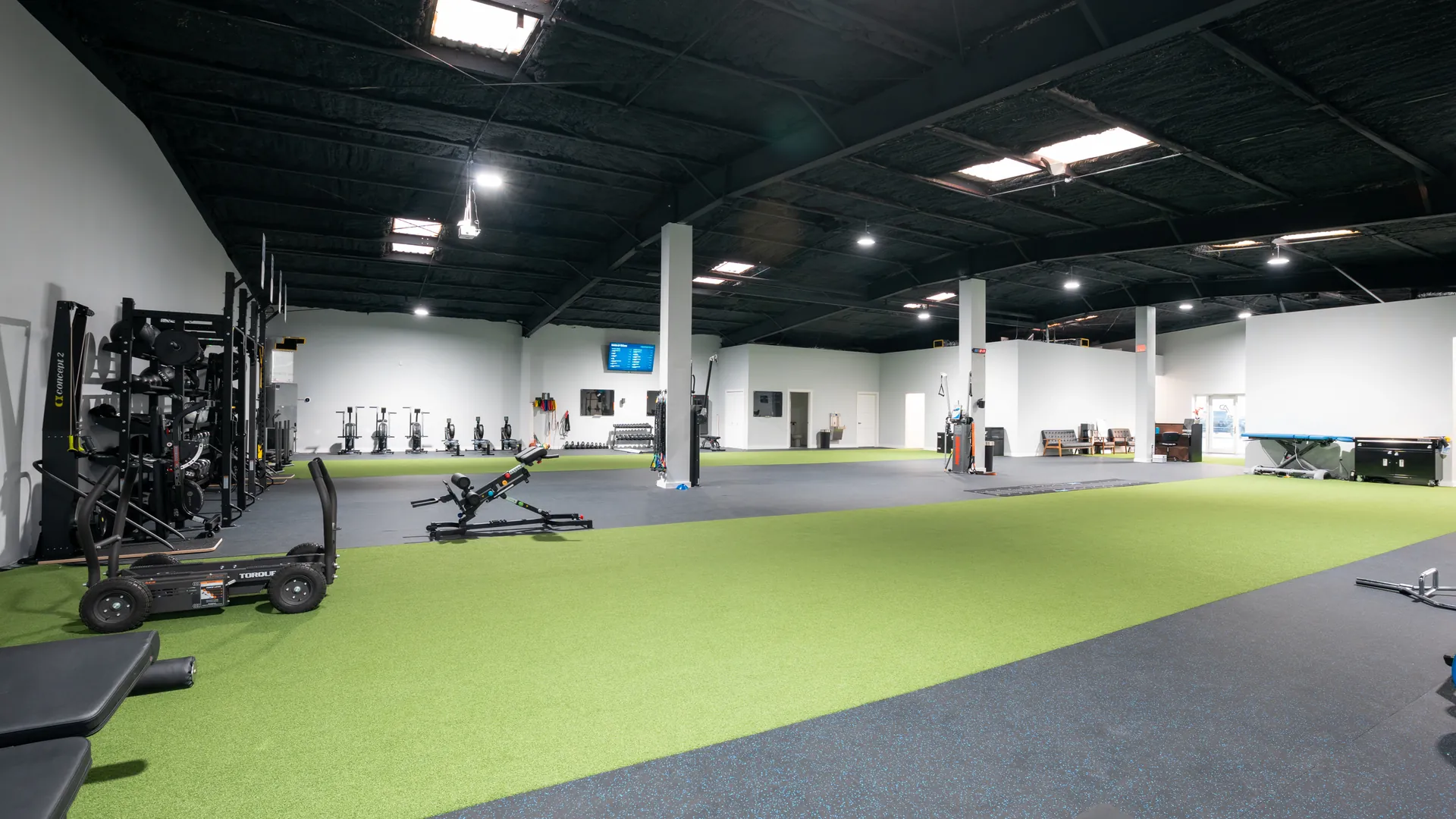 Wide view of the Athlete Pro training floor with turf, equipment racks and a dark industrial ceiling
