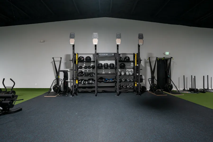 Wide view of the Athlete Pro training floor with a rack wall, medicine balls and turf under a dark ceiling