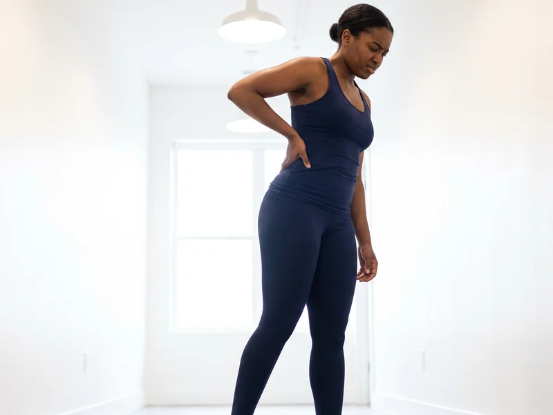 Close-up of a person holding their lower back and hip while bending forward in discomfort