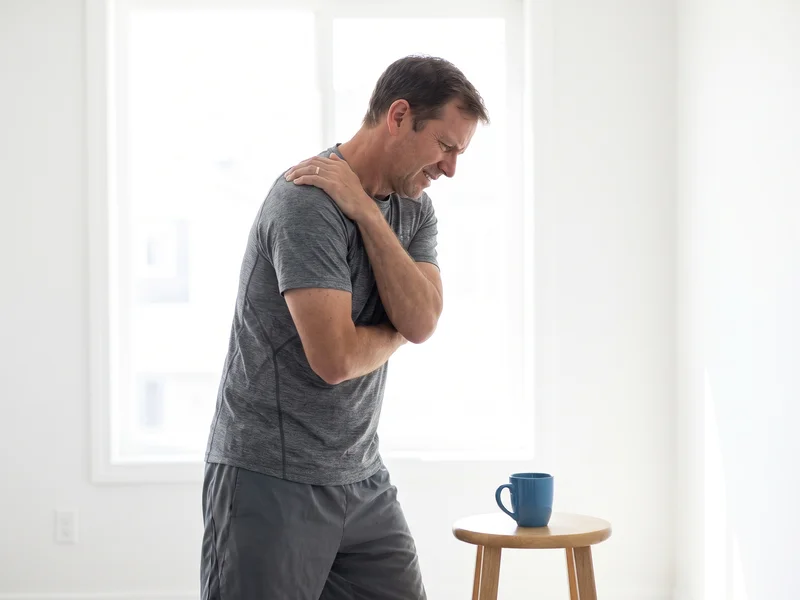 Close-up of a person gripping their shoulder in discomfort